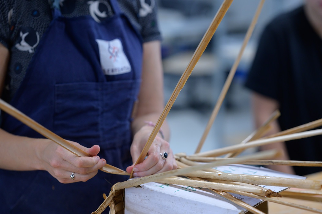 A close-up of the hands of a person weaving something out of bulrush