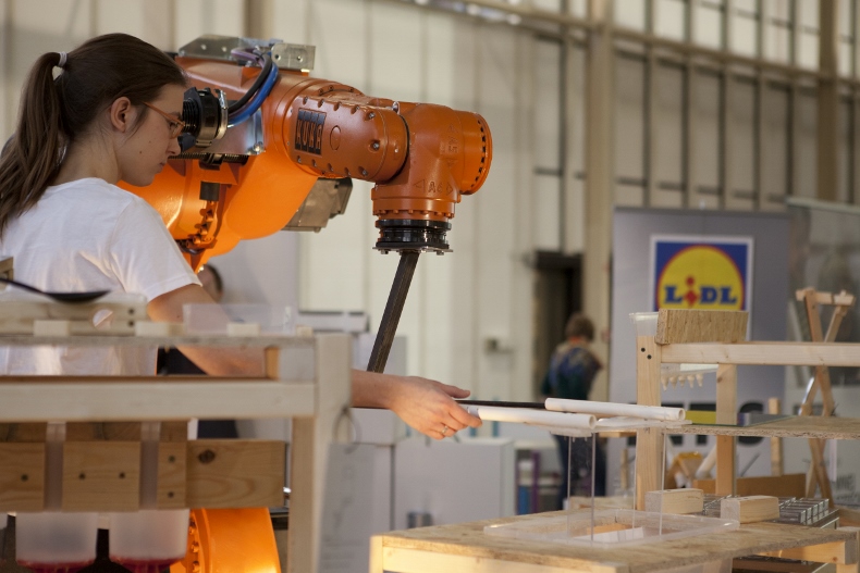 A girl in the workshop operates a KUKA industrial robot.