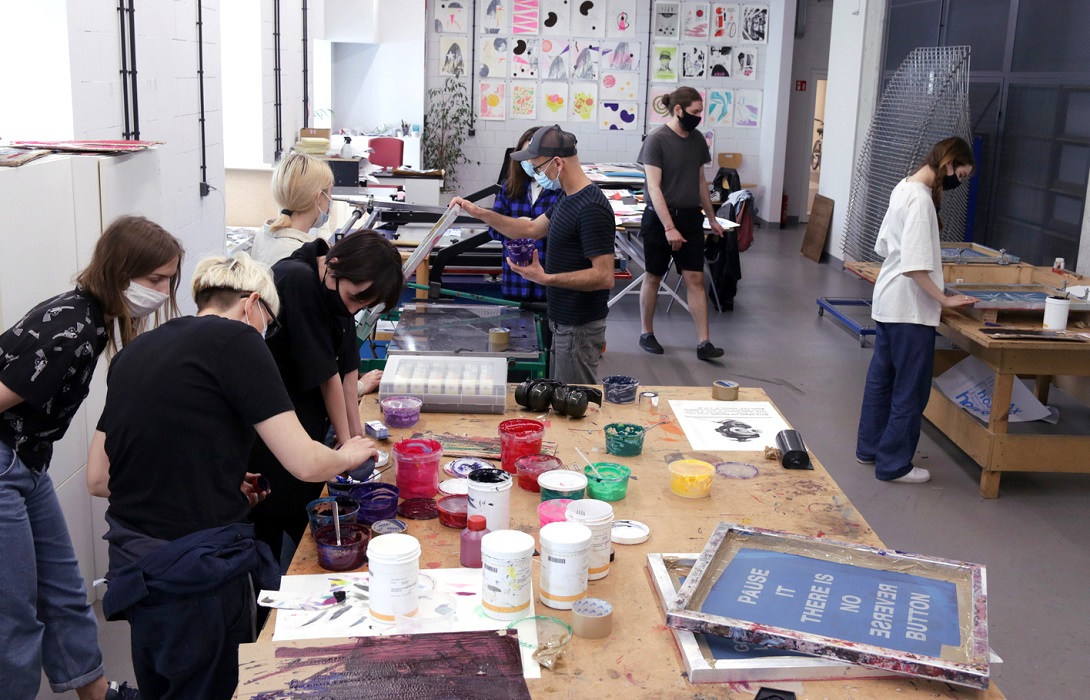 A group of students in the studio mix paints and prepare screen prints