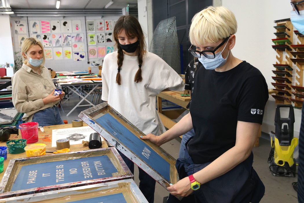 A woman is looking at a screen print made by a student