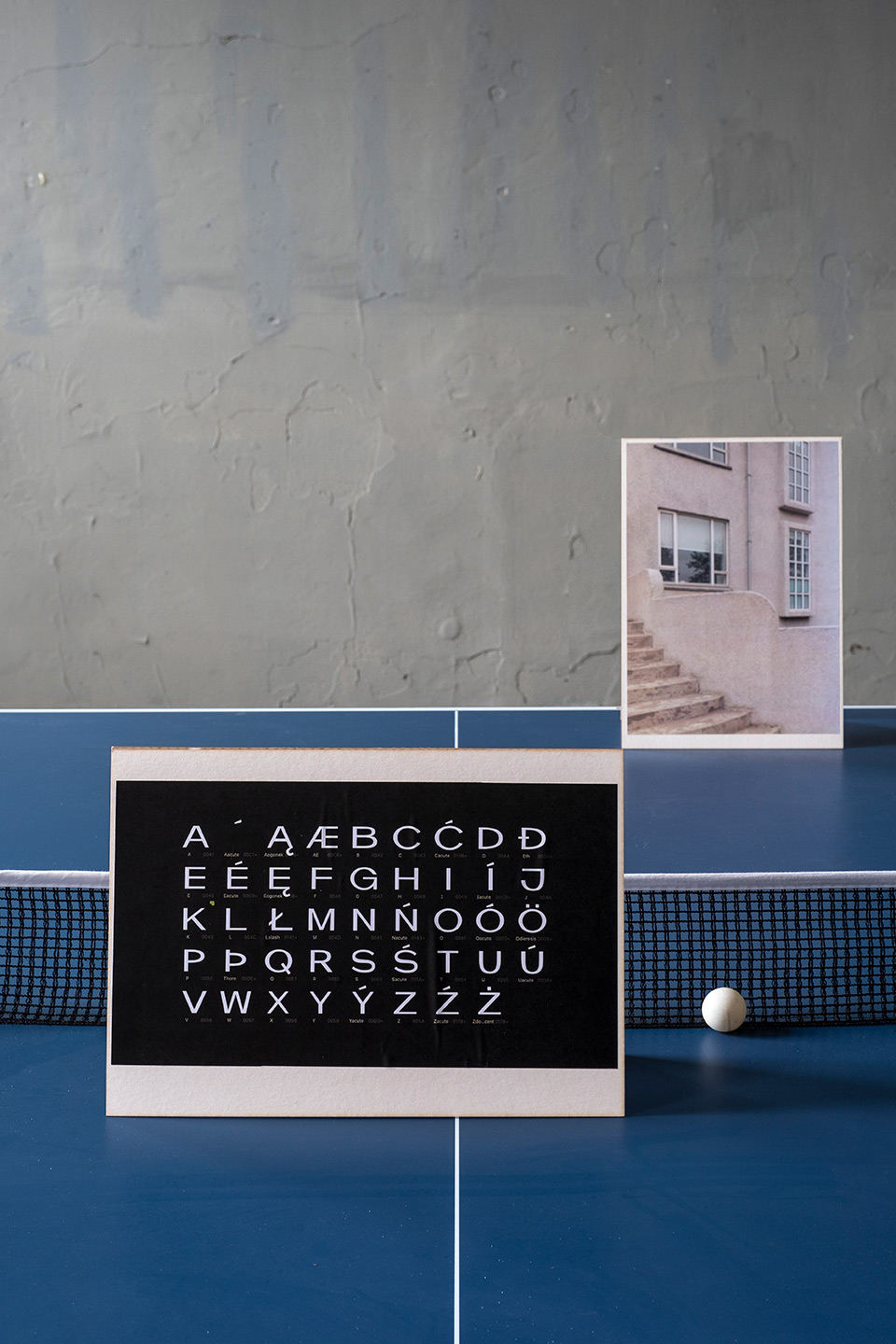 Karty ze zdjęciami architektury islandzkiej z nadrukowanymi literami z islandzkiego. Karty są położone na stole do ping ponga. 
