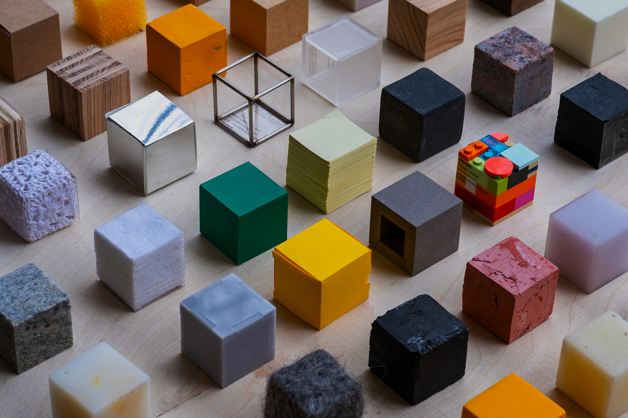 Zbiór tej samej wielkości sześcianów wykonanych z różnych materiałów, m.in. z metalu, papieru, plastiku, klocków lego.