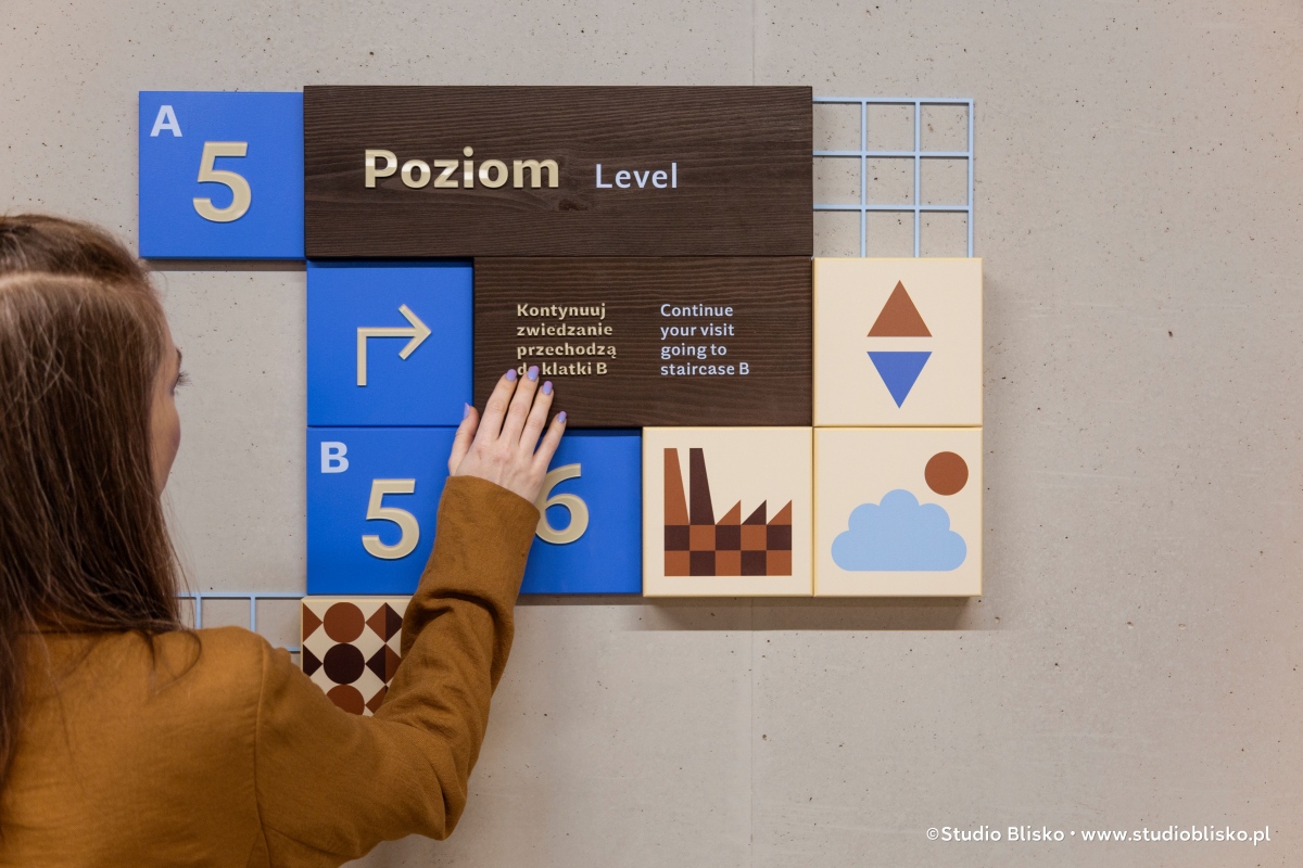 A woman points to a tile on the modular wayfinding signage at the Chocolate Factory museum