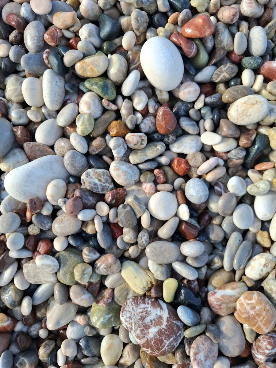 Zbliżenie na różnokolorowe, gładkie otoczaki o różnych rozmiarach leżące na plaży.