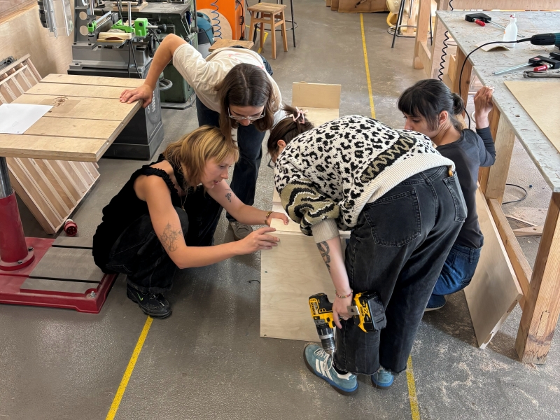 Group of School of Form students leaning over a piece of furniture, discussing the design.