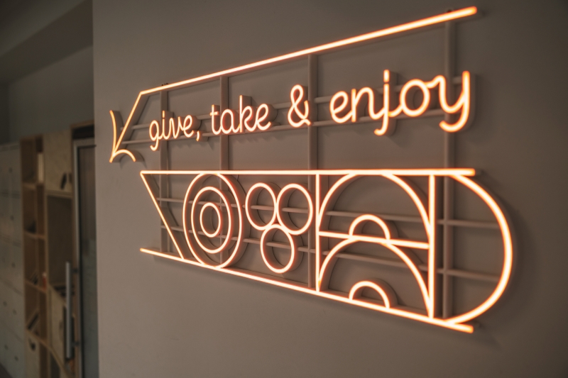 LED sign reading “Give, take & enjoy” marking the location of the food sharing corner at SWPS University.