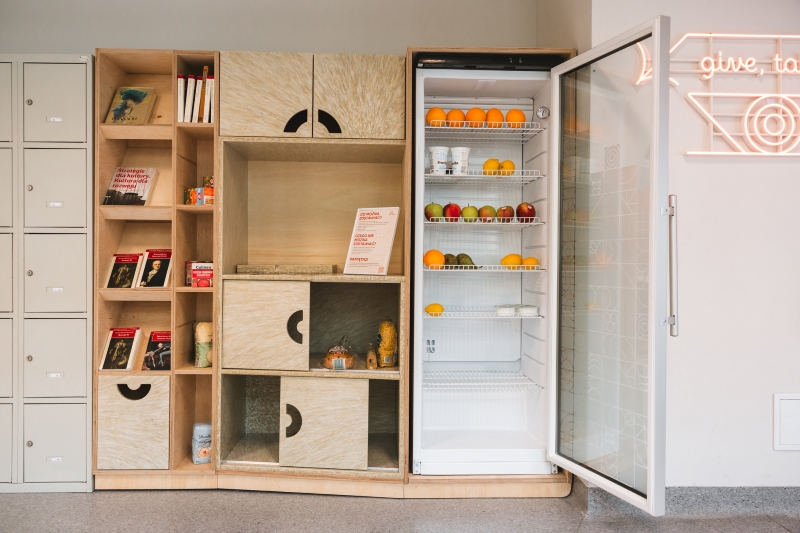 Food sharing corner at SWPS University, front view of shelves and an open fridge with fruit inside.