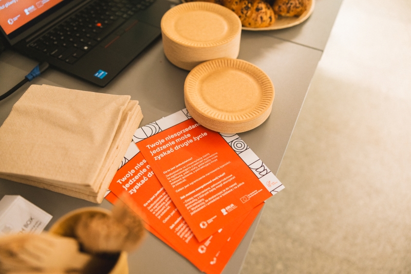 Close-up of a table with flyers promoting food waste reduction, and paper tableware.