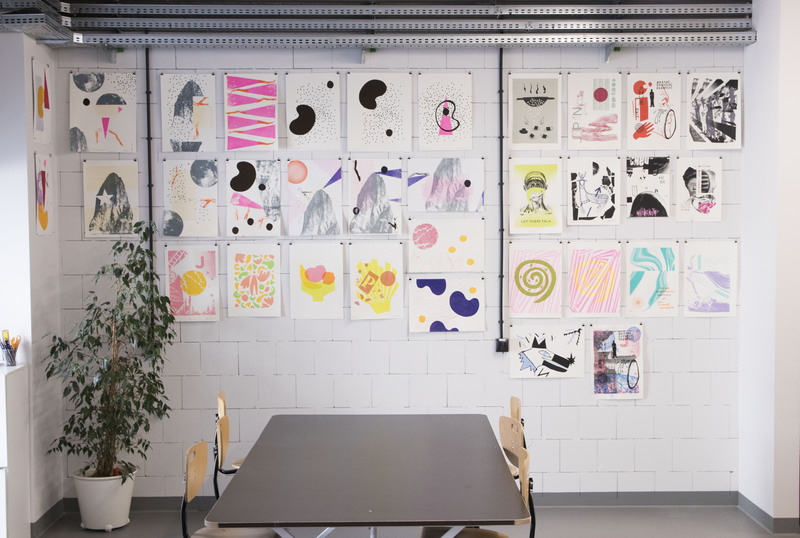 Biała ceglasta ściana z projektami graficznymi studentów