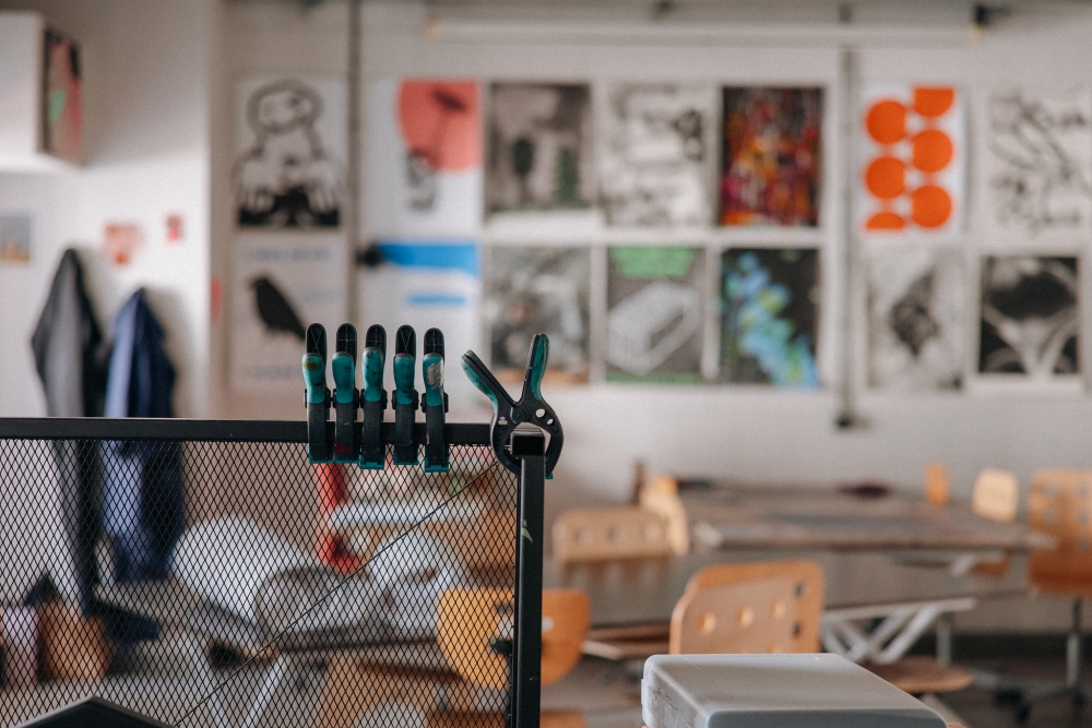 Widok na jedną ze ścian w pracowni sitodruku; w tle wiszą prace wykonane w technice sitodruku