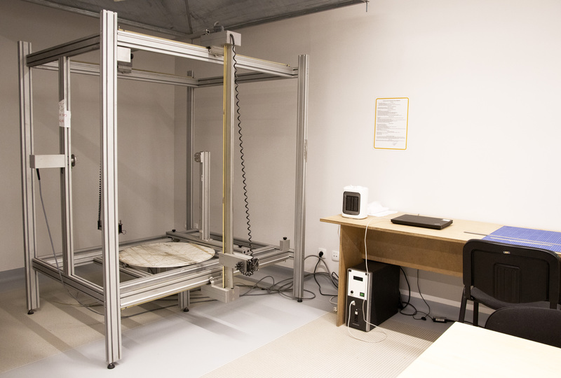 Wnętrze pracowni - wielkoformatowa drukarka 3D stojąca w rogu pokoju