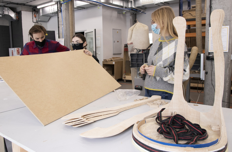 Young girl in woodworking workshop holds chipboard and discusses project with lecturer