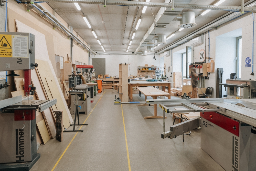 Interior of the woodworking workshop, with various machines and wooden boards standing against the walls.