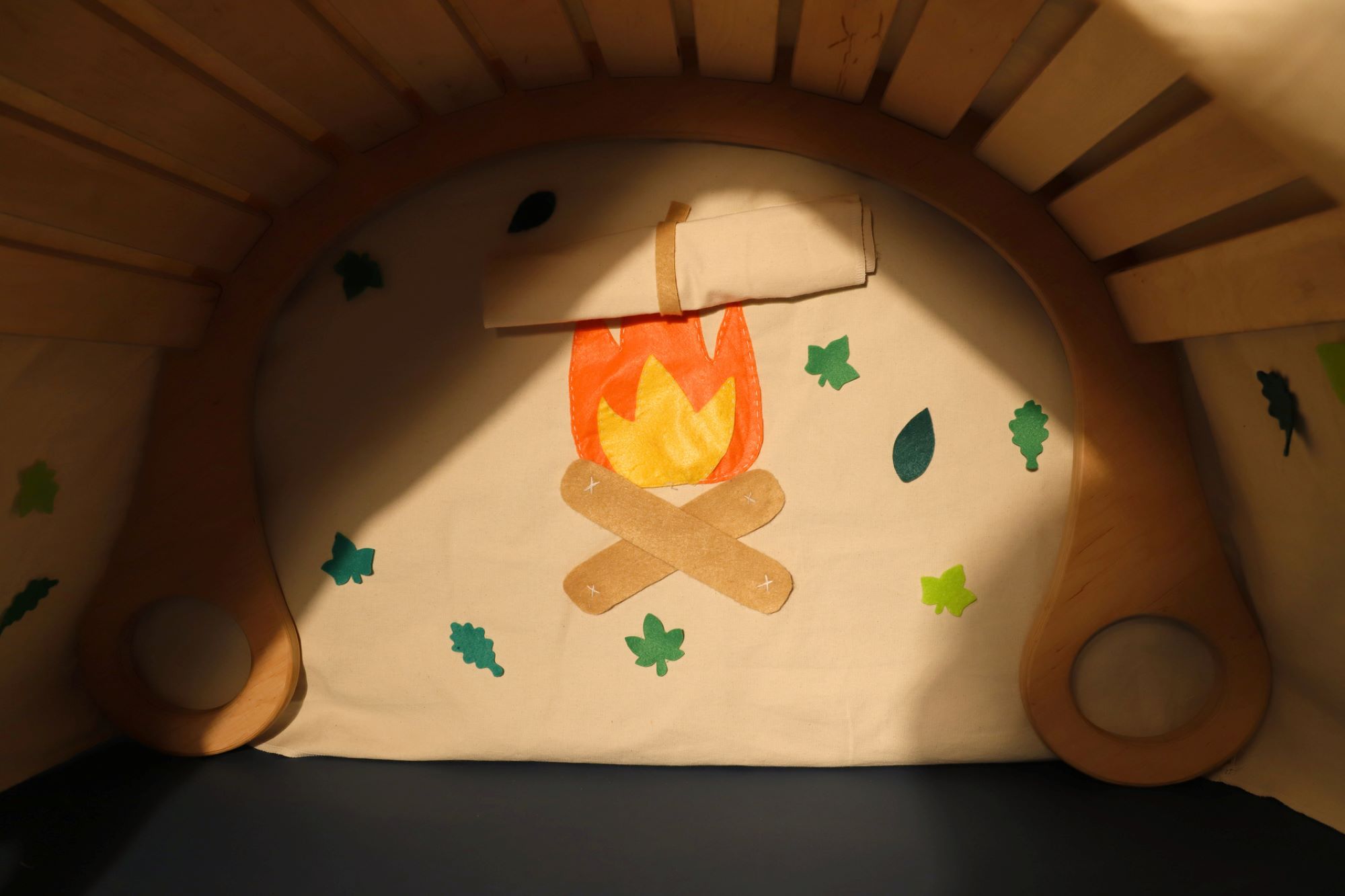 Rocker with accessories that transform it into a tent; decorative elements shaped like a campfire and leaves are attached to the back wall