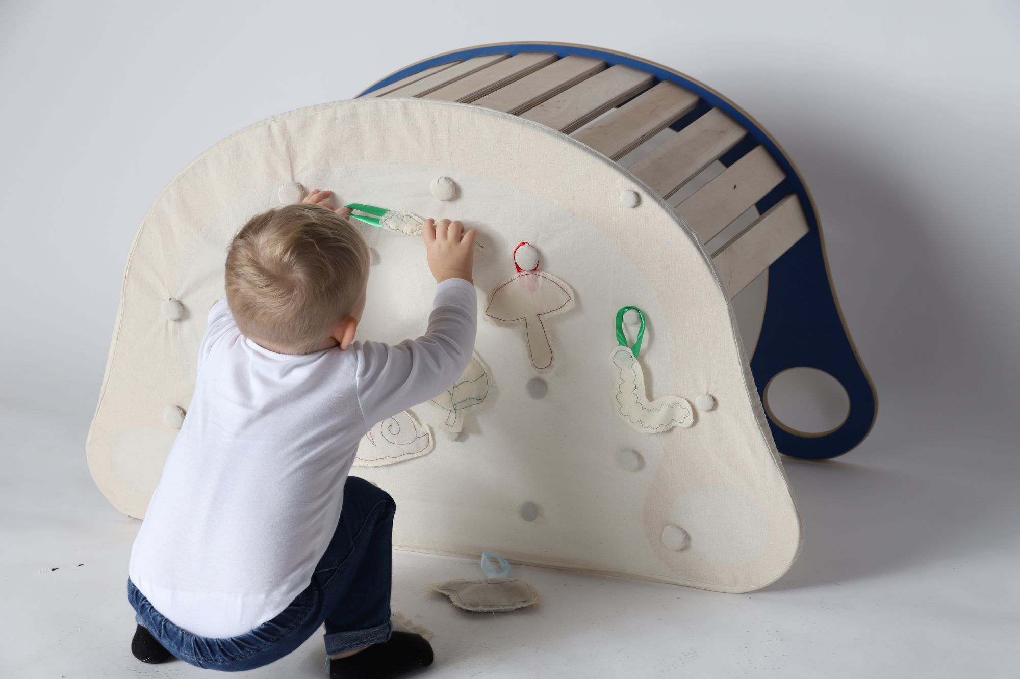 Rocker covered with a fabric sheet; a small child attaches plush plant toys to it