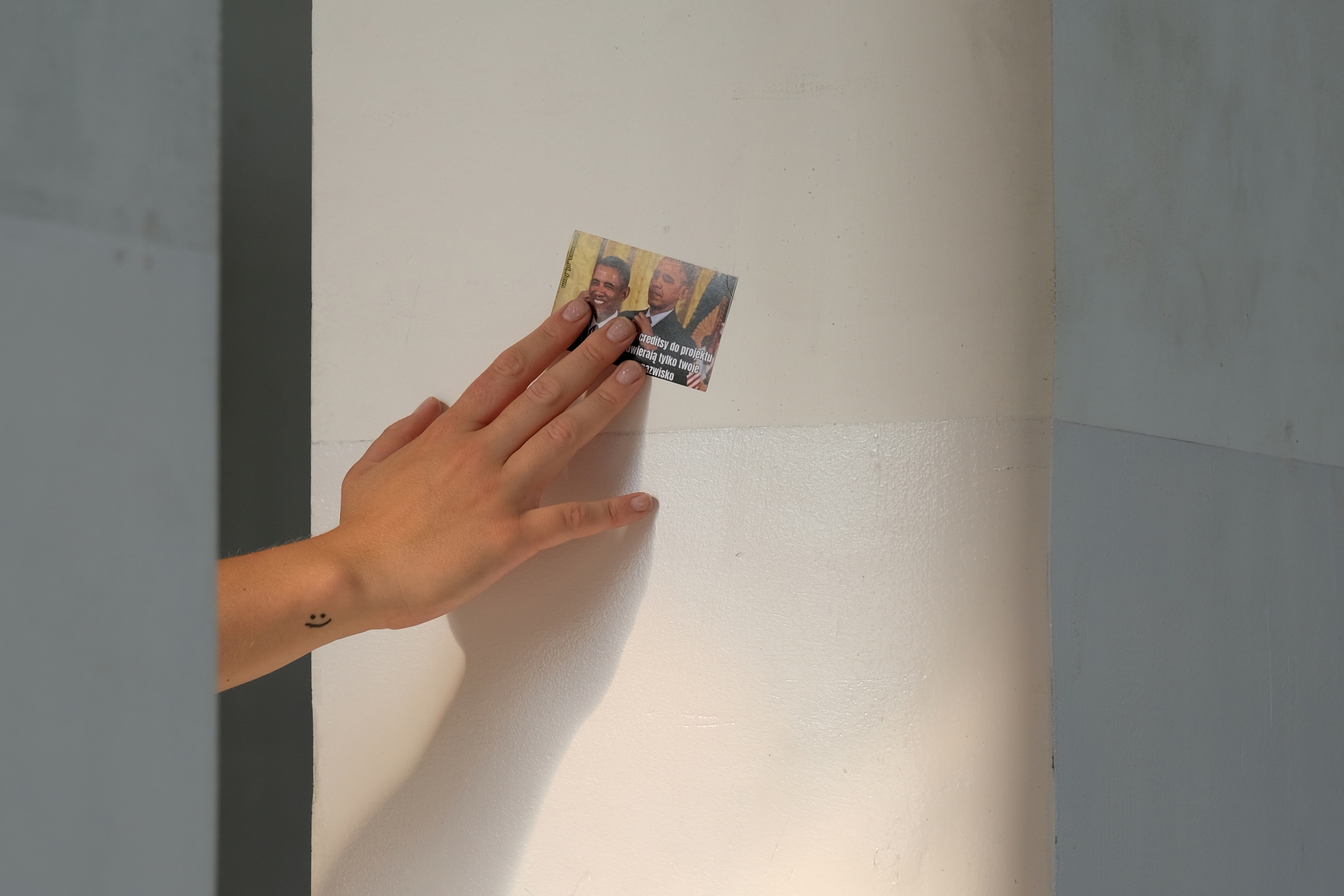 A woman's hand places a sticker with a meme image on the wall.