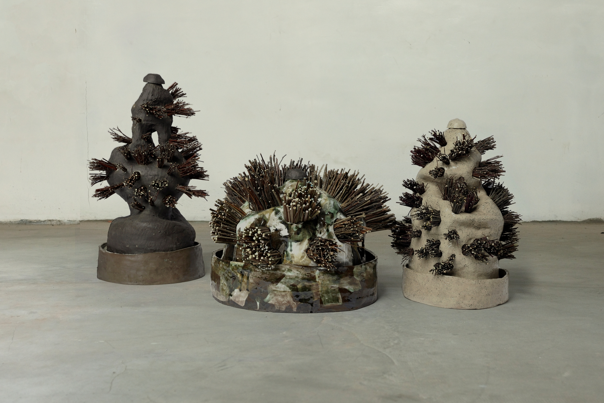 Three clay objects resembling succulents stand on a concrete floor.