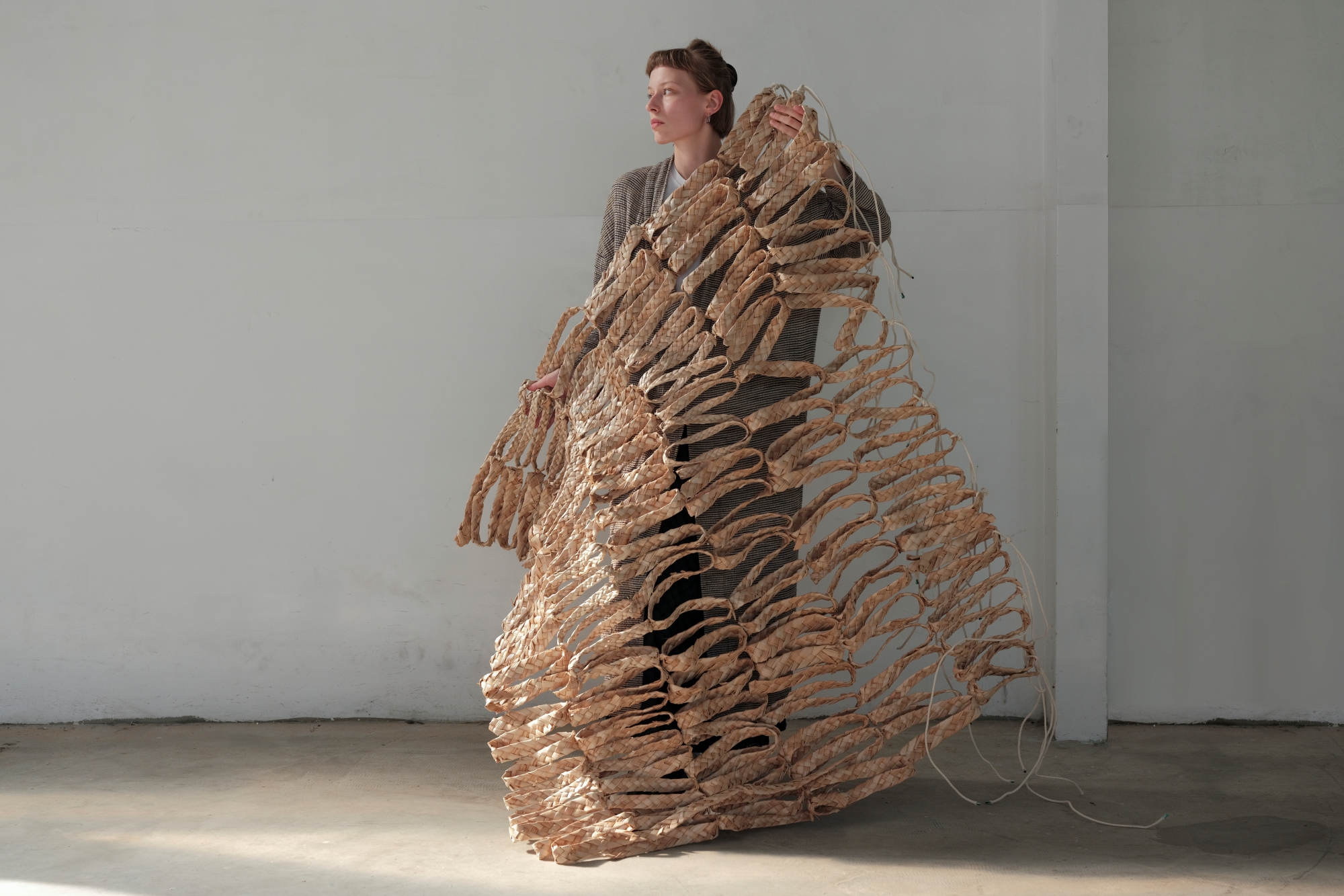 A young woman holds a window installation resembling a net, crafted from natural materials by Zofia Kusch.