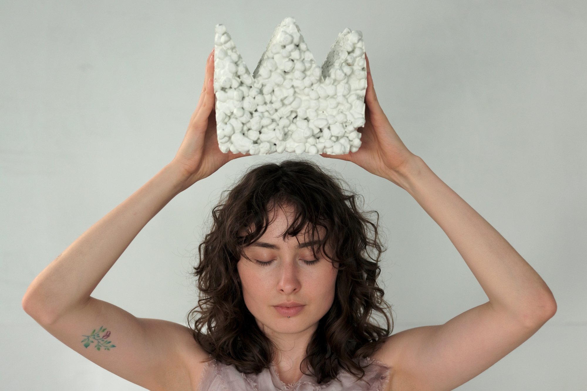 A young woman holds a crown-shaped object above her head.
