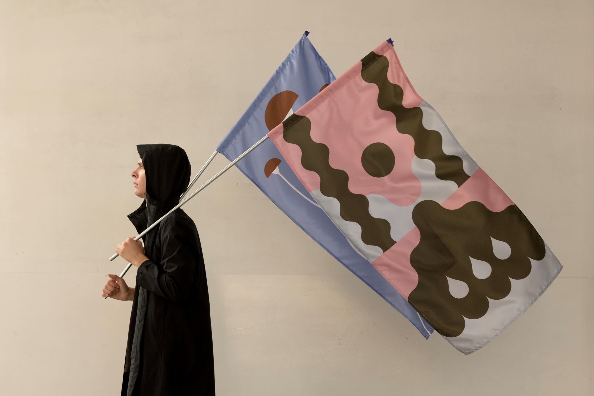 A man in a black coat carries colorful flags with abstract patterns.