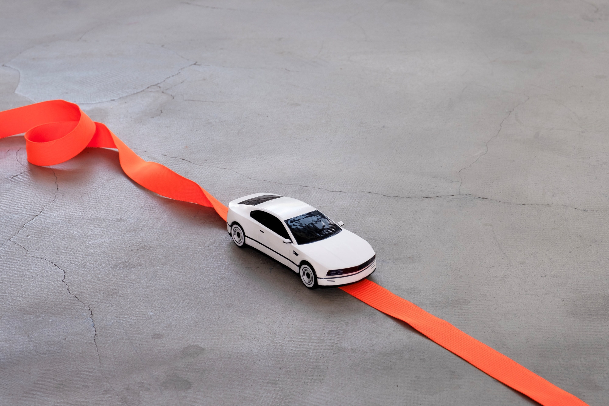 A model car designed by Ilia Matiazh, placed on a concrete floor, with a ribbon simulating a traffic lane