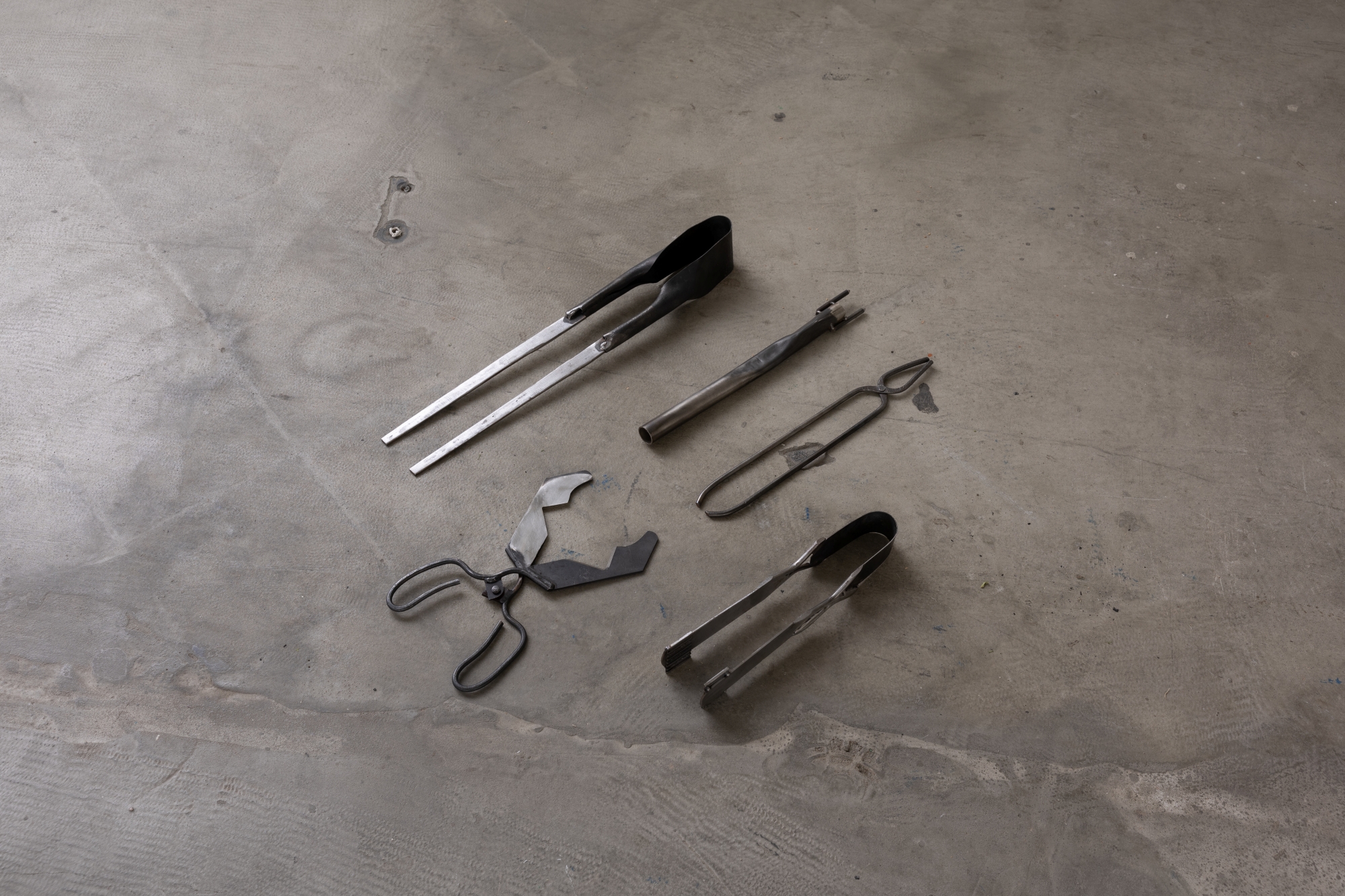 Five glassblowing tools on a concrete floor