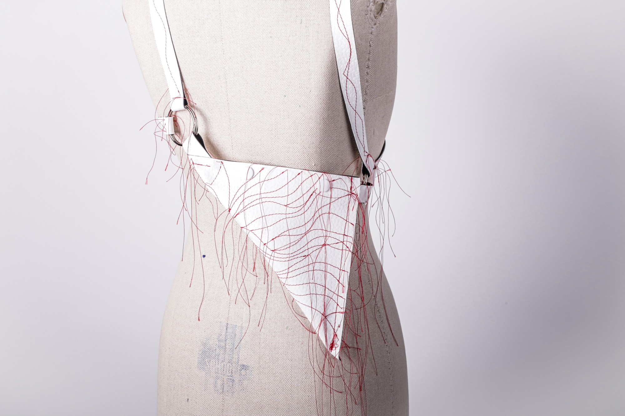 A small bag made of roofing membrane, decorated with thin cords resembling nerve fibers, displayed on a mannequin.