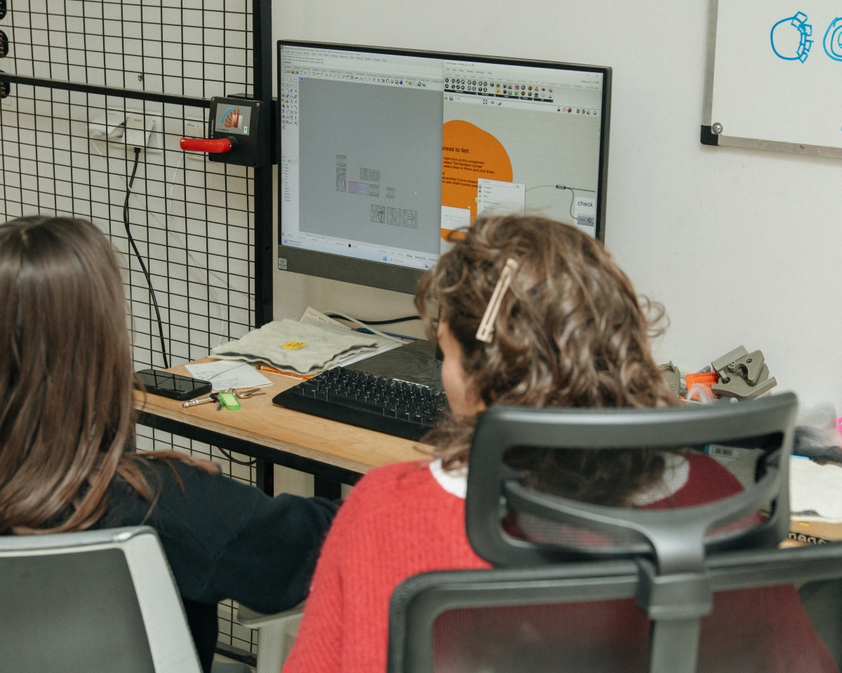 Dwie osoby siedzą przed monitorem komputera, na którym otwarty jest program do projektowania przestrzennego z widocznymi schematami i wzorami do filcowania.