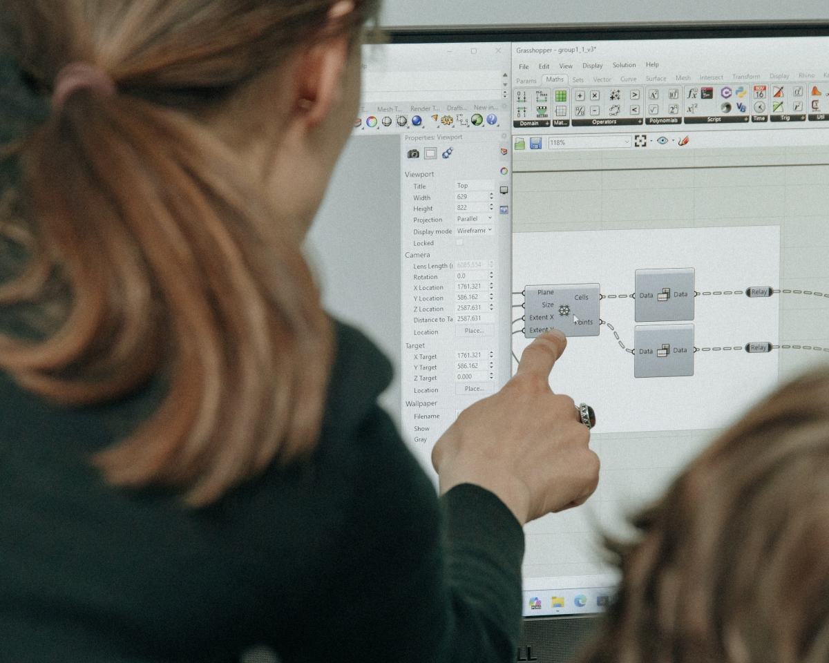 Zbliżenie na monitor komputera z widocznym interfejsem programu do projektowania algorytmicznego. Dłoń osoby wskazuje palcem na konkretny blok z parametrami.