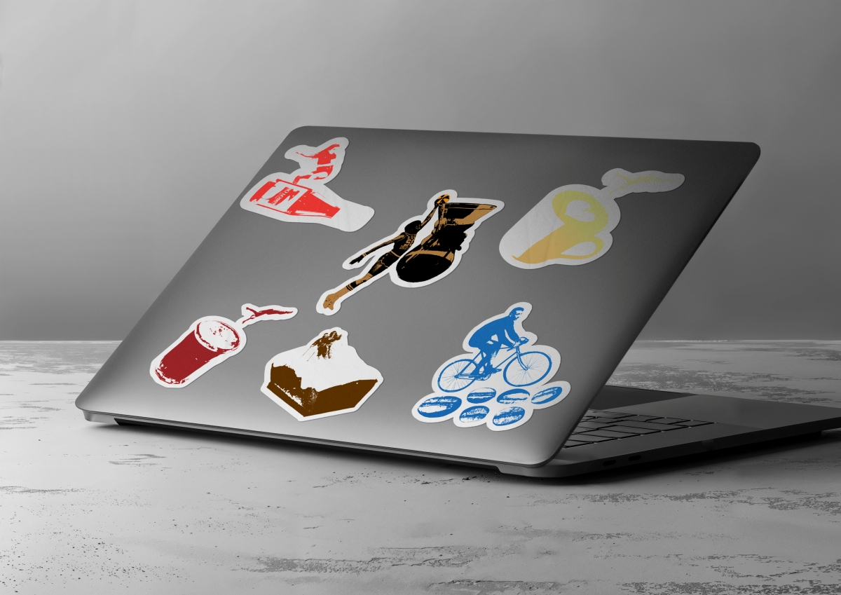 Naklejki na obudowie laptopa. Grafiki łączą motywy sportowe z kawiarnianymi, ukazują m.in. narciarza na ciastku, rowerzystę jadącego po ziarnach kawy oraz koszykarza wrzucającego piłkę do zaparzacza.