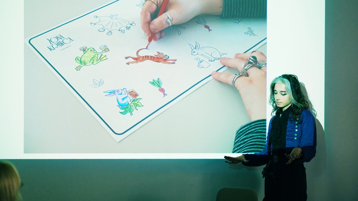A School of Form student stands next to a screen during a presentation. The displayed slide features sticker designs of animals with café accessories.